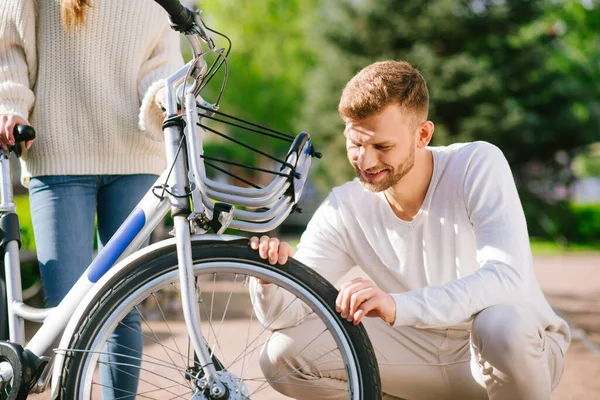 Szakállas férfi nézi a kerék és a nő támogató kerékpár — Stock Fotó