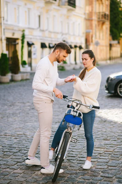 Uomo esaminando braccio donne in piedi con bicicletta — Foto Stock