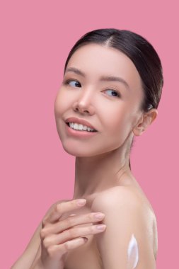 Genç kadın banyo yaptıktan sonra vücut losyonu kullanıyor.