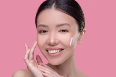 Gülümseyen kadın cildini nemlendirdiği için yüz kremi sürüyor.