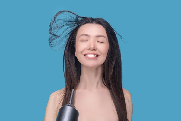 Smiling young woman using a hair dryer — Stock Photo, Image