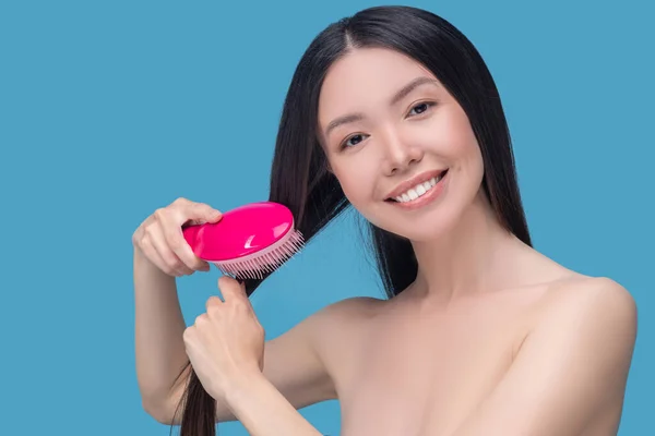 Усміхнена молода жінка чистить її довге волосся — стокове фото