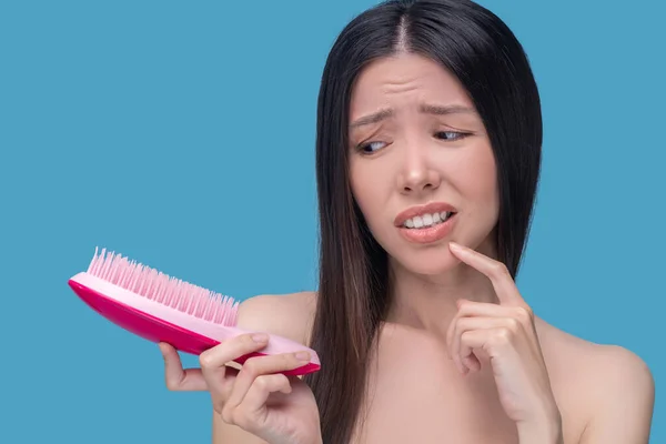 Verwirrte Frau blickt auf die rosa Haarbürste — Stockfoto