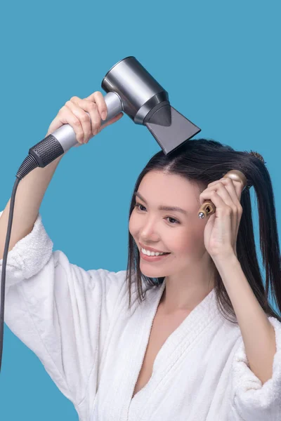 Mujer sonriente peinándose el pelo con un secador de pelo — Foto de Stock