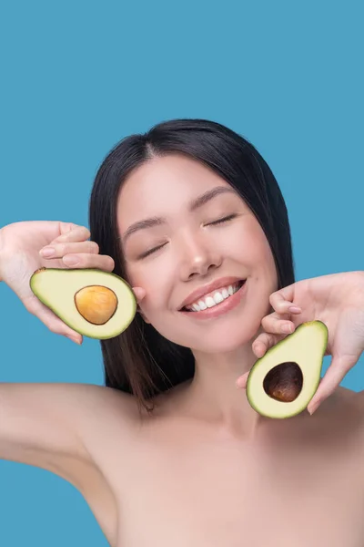 Mujer feliz sosteniendo dos pedazos de aguacate maduro — Foto de Stock