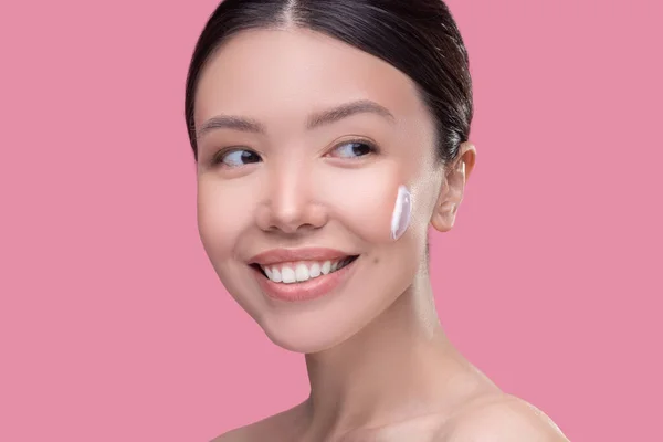 Donna sorridente che prova nuova crema viso sulla sua pelle — Foto Stock