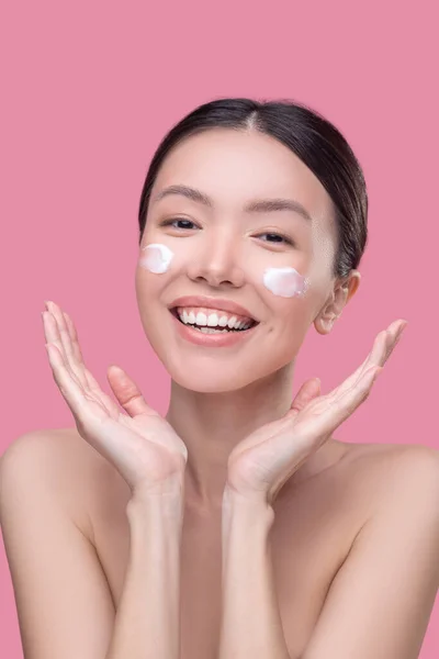 Mujer sonriente protegiendo su piel con crema facial —  Fotos de Stock