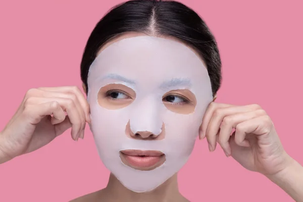 Femme appliquant un masque textile de soins de la peau sur son visage — Photo