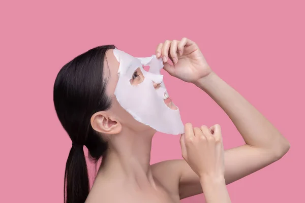 Wanita muda menerapkan masker kecantikan wajah tekstil — Stok Foto