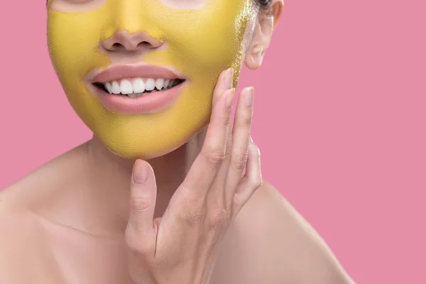 Mujer aplicando novedosa mascarilla dorada a su piel —  Fotos de Stock