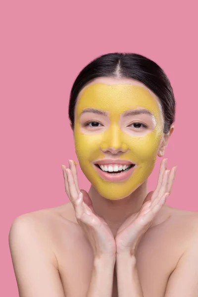 Mujer joven sonriente aplicando mascarilla dorada — Foto de Stock