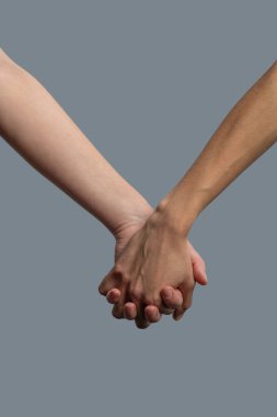 Açık tenli ve koyu tenli insanların el ele tutuşması.