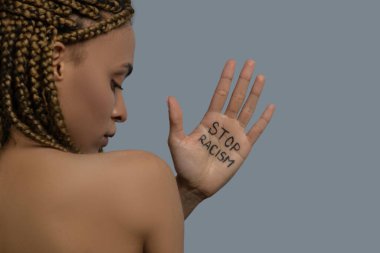 Young African American woman standing back to camera, showing palm with stop racism lettering above her shoulder clipart