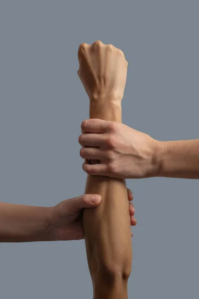 Close-up de duas mãos de pele clara segurando pulso e antebraço de mão de pele escura — Fotografia de Stock