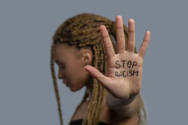 Young African American woman standing sideways, head down, showing palm with stop racism lettering — Stock Photo, Image