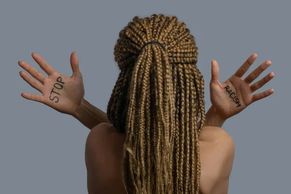 Young African American woman standing back to camera, showing palms with stop racism lettering above her shoulders