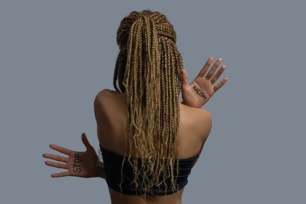 Young African American woman in black top standing back to camera, showing palms with stop racism lettering — Stock Photo, Image