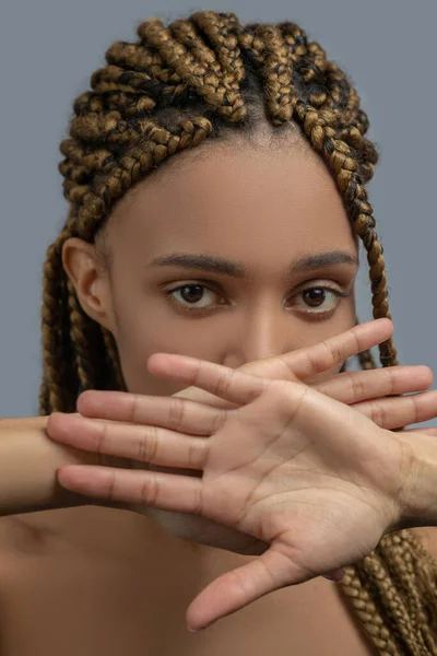 Сумно, що молода афроамериканка закриває рота перехрещеними руками, показуючи пальцями фотоапарат. — стокове фото