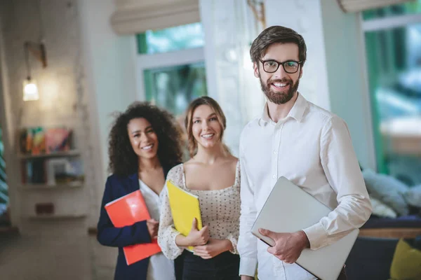 Lächelnder Kerl mit Laptop und zwei Mädchen mit Notizbüchern. — Stockfoto