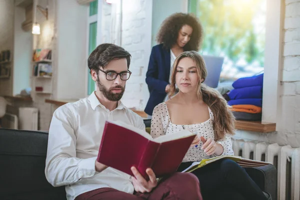 Bearded guy reading book and two girls.