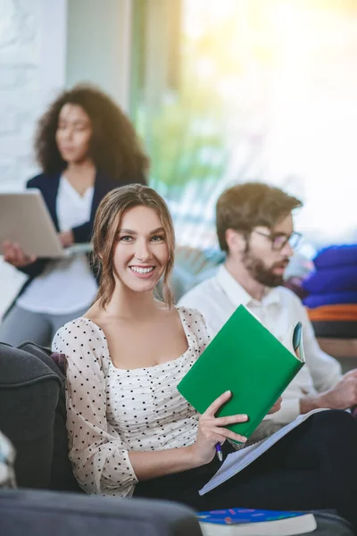 Mädchen mit Buch blickt in die Kamera, Freunde in der Ferne beschäftigt — Stockfoto