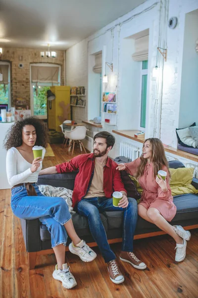 Guy och två tjejer med kaffe sittandes på soffan — Stockfoto