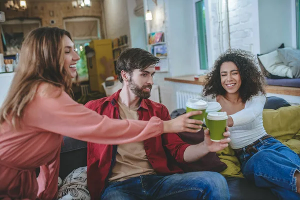 Tres amigos en el sofá con vasos de café extendidos el uno al otro — Foto de Stock