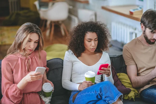 Tres amigos adultos jóvenes mirando con sus teléfonos inteligentes en el sofá —  Fotos de Stock