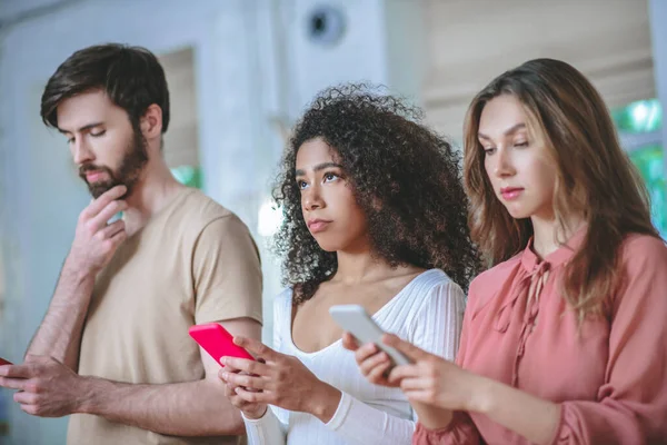 Jóvenes involucrados de pie con teléfonos inteligentes en las manos —  Fotos de Stock