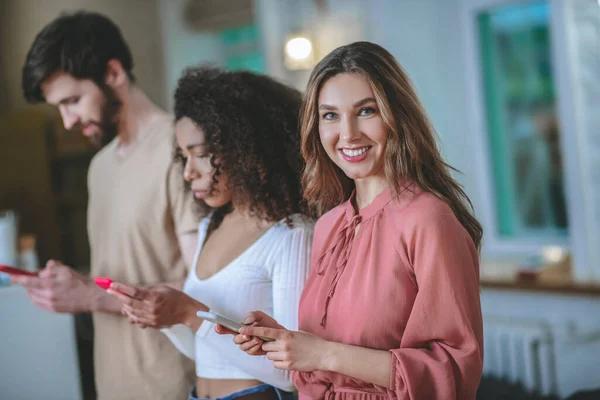 Chica sonriente en vestido rosa, novia con novio mirando los teléfonos inteligentes — Foto de Stock