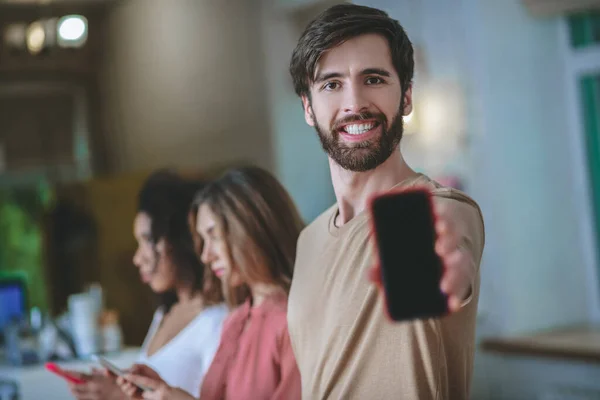 Sonriente hombre sosteniendo teléfono inteligente en el brazo extendido, dos chicas detrás —  Fotos de Stock