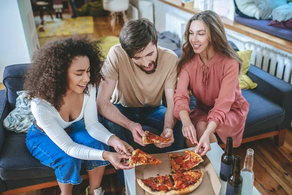Três jovens amigos tirando um pedaço de pizza da caixa — Fotografia de Stock