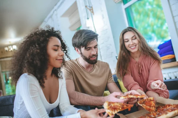 Guy och två tjejer tar pizza från lådan. — Stockfoto