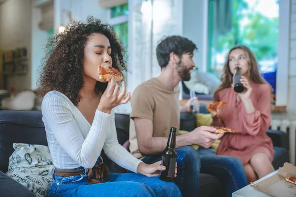 Menina com olhos fechados mordendo sua pizza, namorado com namorada nas proximidades — Fotografia de Stock