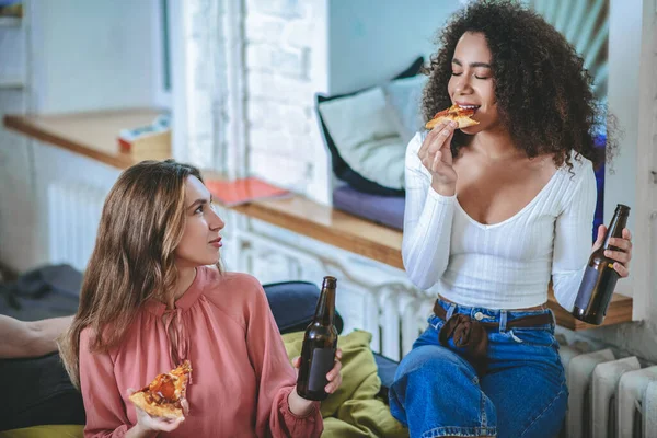 Duas namoradas com pizza e garrafas comunicando no quarto — Fotografia de Stock