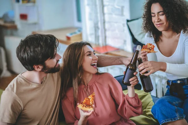 Duas garotas com pizza e cara segurando garrafas uma para a outra — Fotografia de Stock