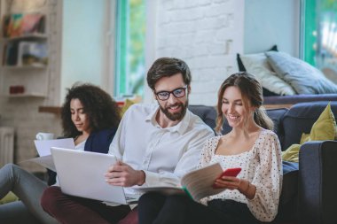 Dizüstü bilgisayarı olan neşeli bir adam ve belgelerle çalışan iki kız.
