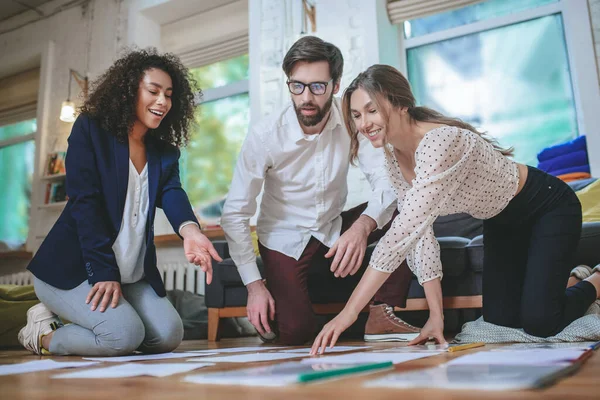 Chico serio y dos chicas sonrientes inclinadas sobre papeles — Foto de Stock