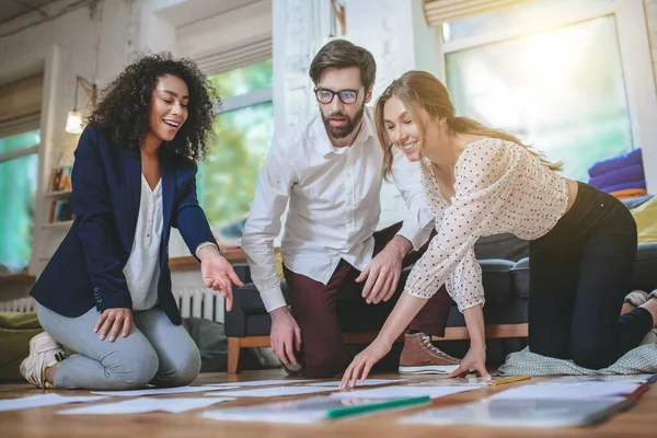 Fröhliche Mädchen und nachdenklicher Kerl legen Dokumente auf den Boden. — Stockfoto