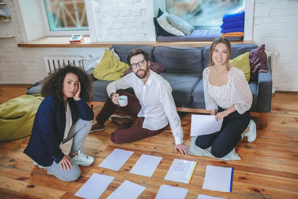 Erfolgreiche zwei Mädchen und ein Mann sitzen mit Dokumenten auf dem Boden. — Stockfoto