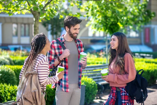 Ragazzo con macchina fotografica e due ragazze con zaini che bevono caffè — Foto Stock