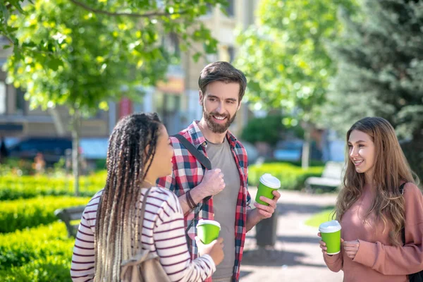 Tre vänner chattar dricka kaffe när de står i parken — Stockfoto