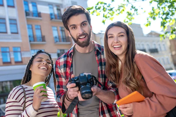 Kille med kamera, två tjejer med kaffe och surfplatta, glad — Stockfoto