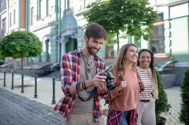 Siyah saçlı adam kameraya bakıyor ve iki kız.