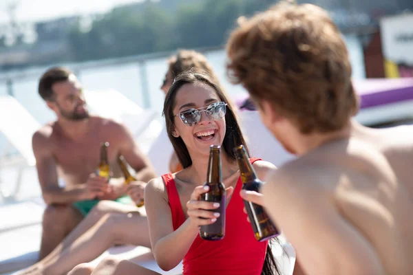 Belle femme aux cheveux bruns en maillot de bain rouge buvant de la bière et parlant à un homme — Photo