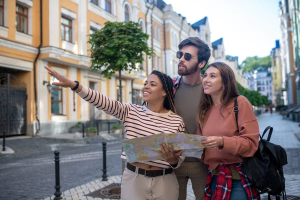 Junger Mann und zwei Mädchen laufen mit Karte durch die Stadt. — Stockfoto