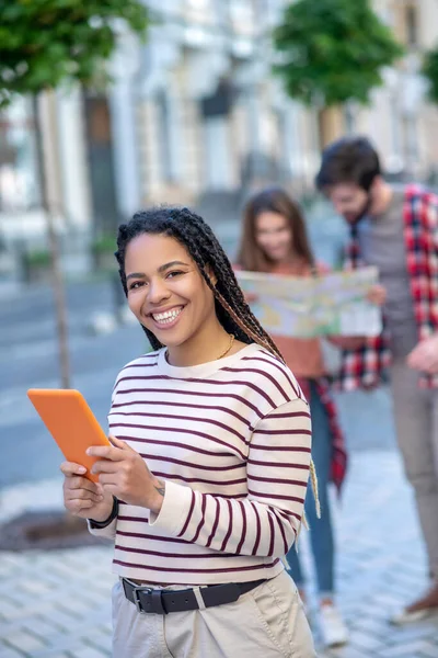 Långhårig mulattflicka med orange tablett i händerna på gatan — Stockfoto