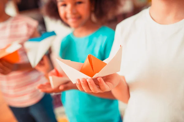 Kid holding an orange origami paper boat