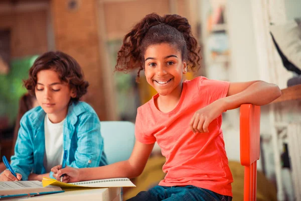 Leende och självsäker flicka skriver sitt uppdrag i klassen — Stockfoto