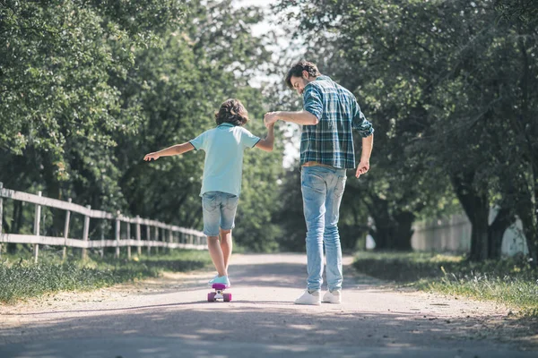 Niño moreno montando un monopatín, su padre lo sostiene — Foto de Stock